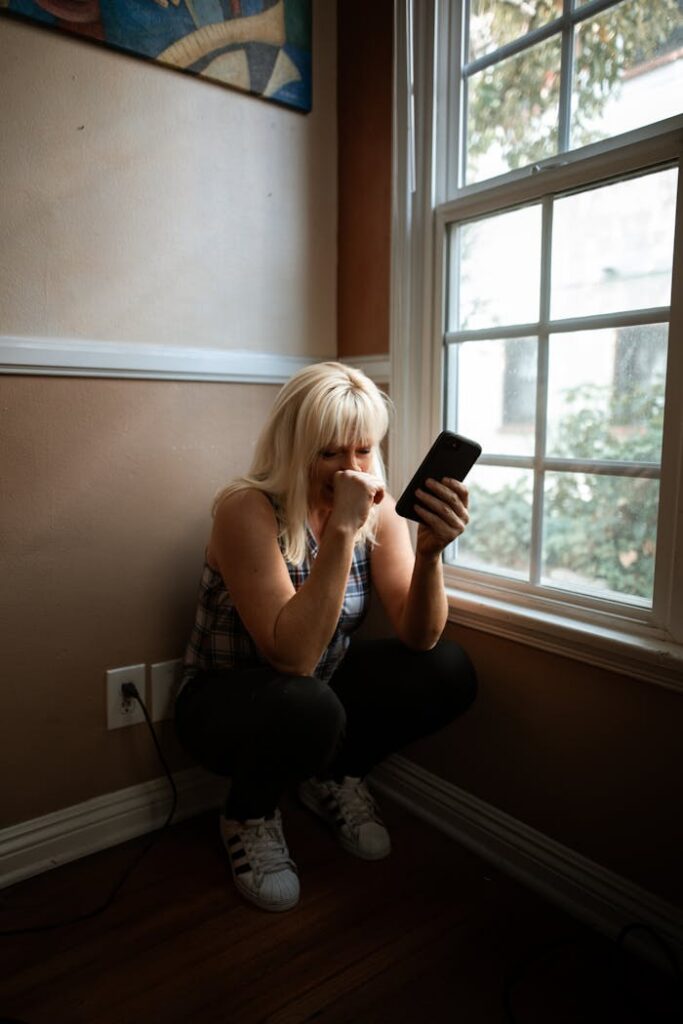 Woman sitting in deep thought by a window, holding a smartphone.